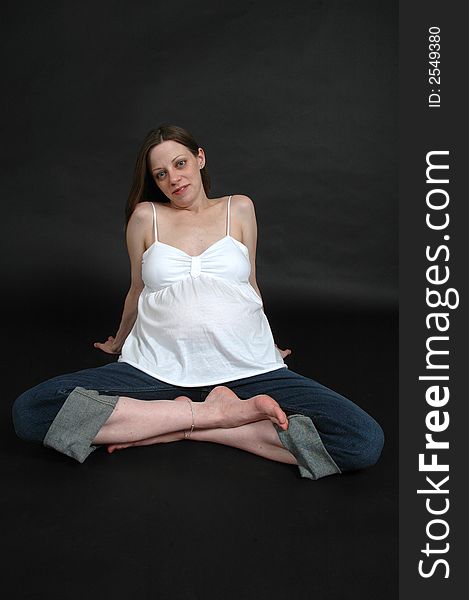 A happy pregnant woman on black background. She is sitting on the floor with her hand on her tummy. A happy pregnant woman on black background. She is sitting on the floor with her hand on her tummy.