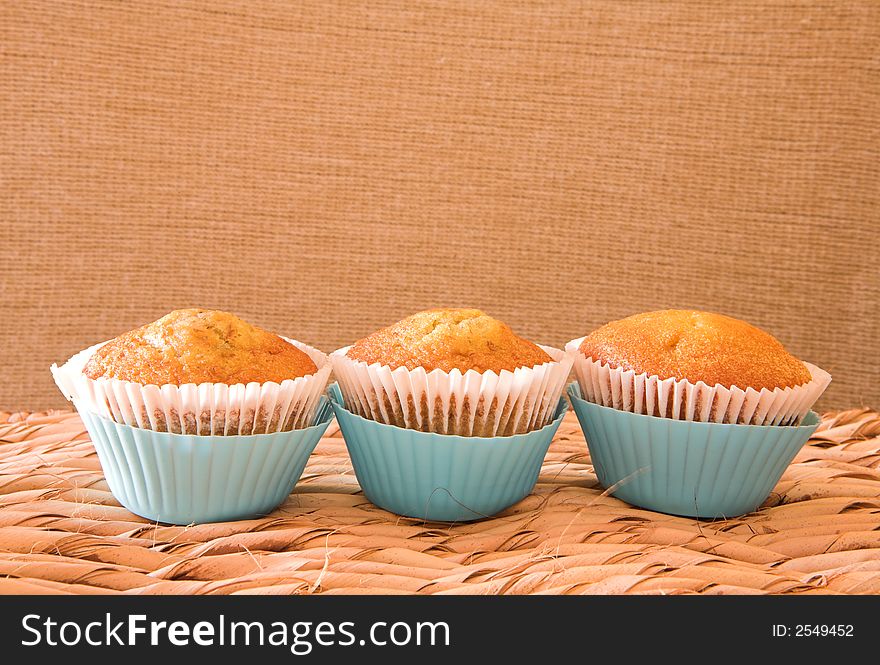 Three carrot muffins in light blue plastic cups against natural wall on grass table. Three carrot muffins in light blue plastic cups against natural wall on grass table