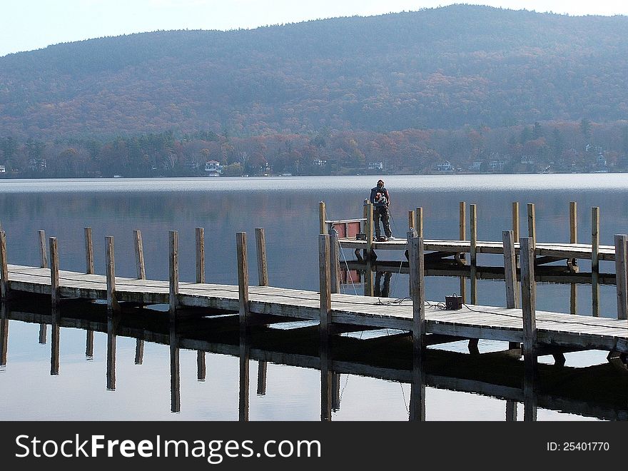 Solitary fisherman out in the early morning hours on a pier at the lake. Solitary fisherman out in the early morning hours on a pier at the lake.