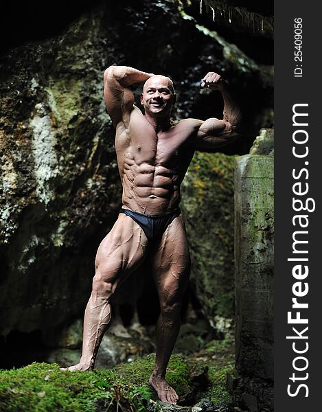 Young bodybuilder posing in a cave