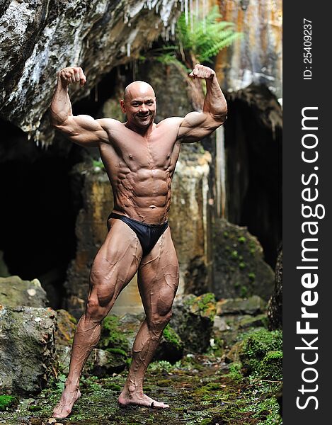 Bodybuilder posing in a cave - Front view