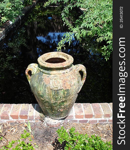 Large clay pot setting on brick wall in front of pond. Large clay pot setting on brick wall in front of pond.