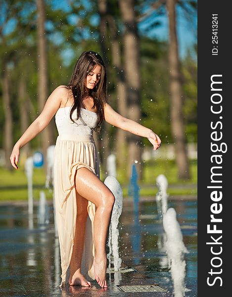 Young beautiful brunette girl playing at outdoor water fountain