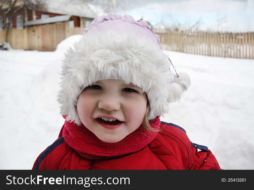 Cute little girl wearing warm clothing stands near home and looks at camera. Cute little girl wearing warm clothing stands near home and looks at camera