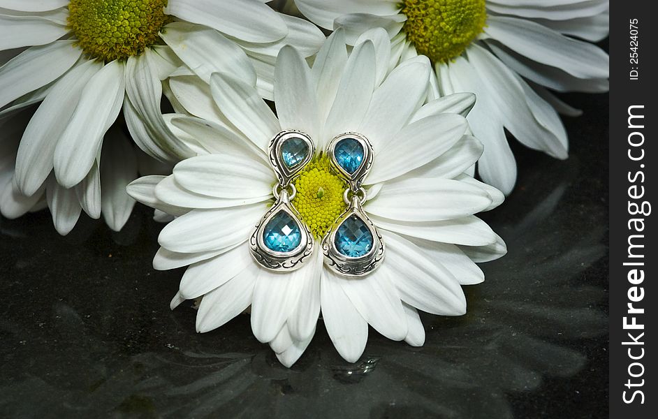 Blue topaz and sterling silver earrings displayed on a white gerbera daisy mounted on polished black granite. Blue topaz and sterling silver earrings displayed on a white gerbera daisy mounted on polished black granite