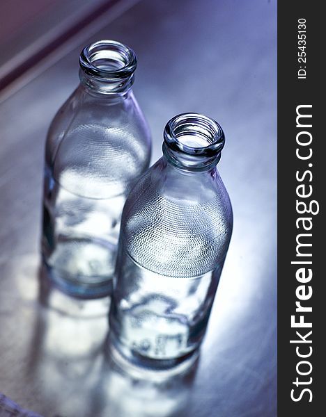 Two empty glass bottle on a mirrored table