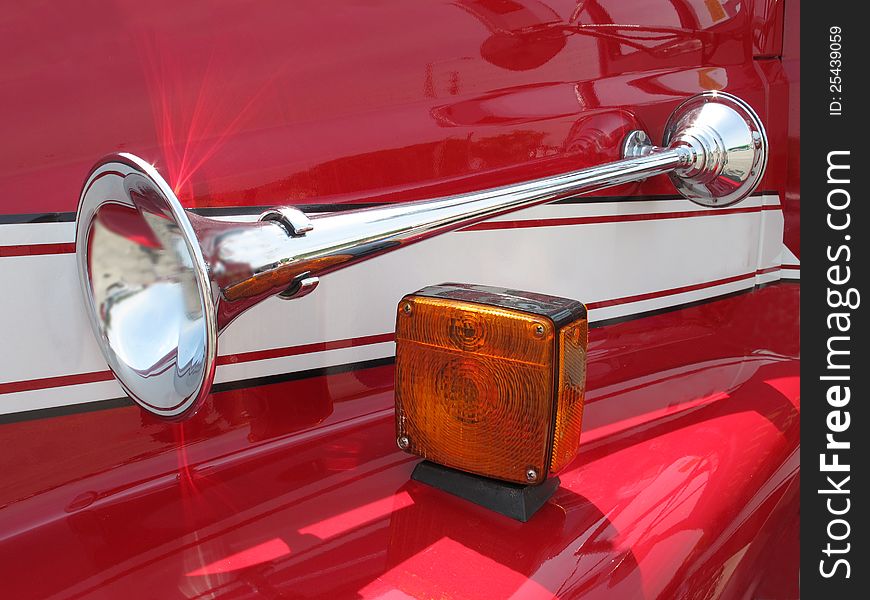 Bright chrome air horn and signal light on the red front fender of a truck. Bright chrome air horn and signal light on the red front fender of a truck.