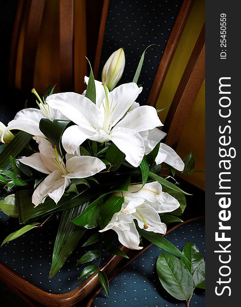 A centrepiece of white lilies, wedding bouquet on dark green chair with dotted pattern