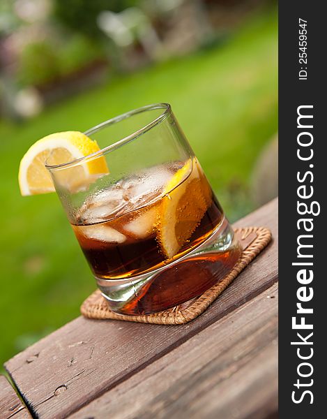 Cocktail in the garden with lemon and ice on a old wooden table in natural light