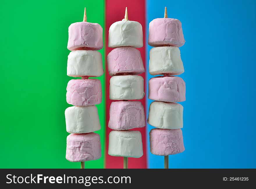 Pink and white marshmallows on skewers with a colorful background.