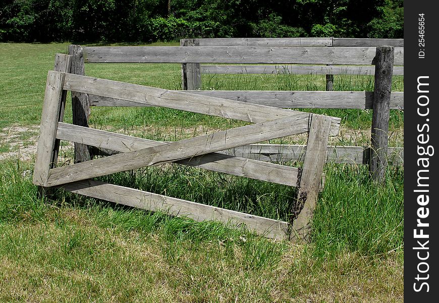 Old weathered gray wood board gate in a pasture, broken off and leaning against a section of fence. Old weathered gray wood board gate in a pasture, broken off and leaning against a section of fence.