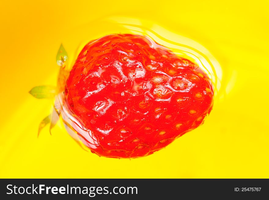 A juicy red strawberry floating on the water against a yellow background. A juicy red strawberry floating on the water against a yellow background