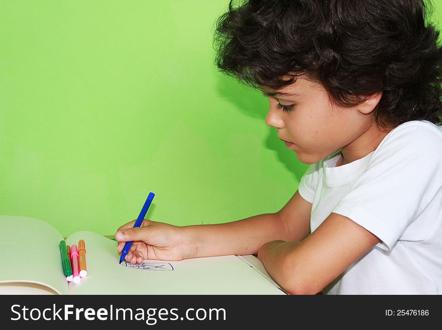 Little curly boy is drawing with colored pencils at home