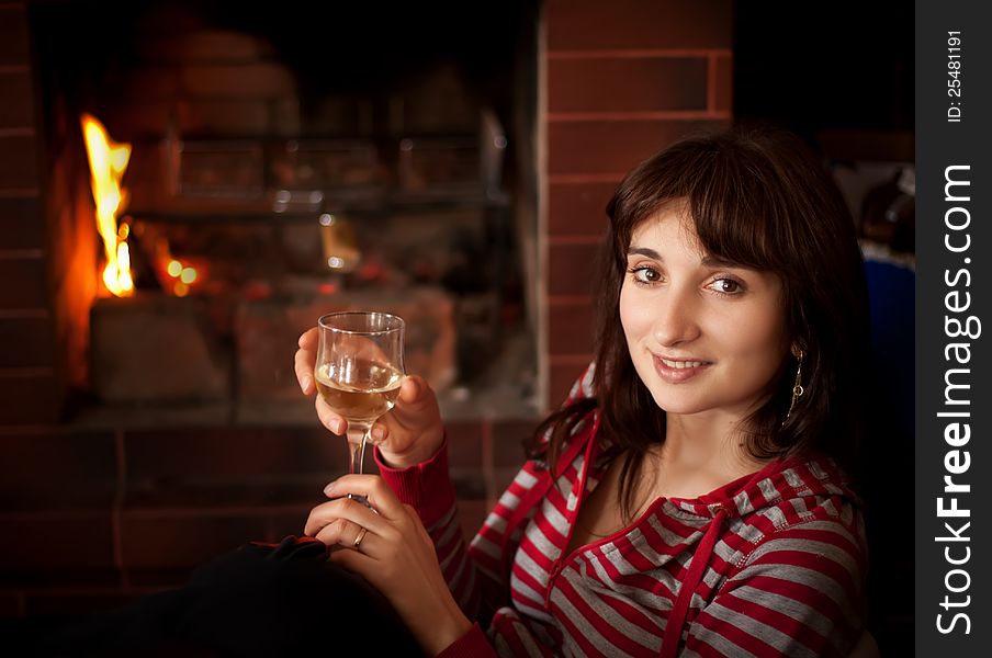 Portrait of a young woman with a glass of wine near the fireplace