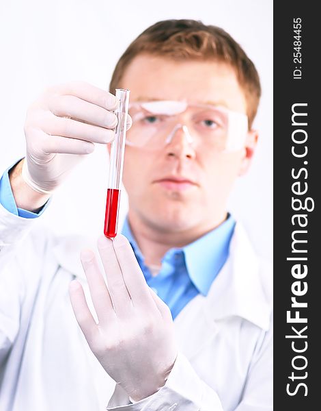 Man in white coat and protective glasses looking at a sample of red liquid test tube. Man in white coat and protective glasses looking at a sample of red liquid test tube