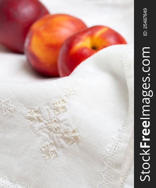 Embroidered detail on white napkin plus three nectarines. Embroidered detail on white napkin plus three nectarines