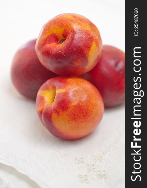 Four nectarines resting on embroidered linen napkin, on white. Four nectarines resting on embroidered linen napkin, on white