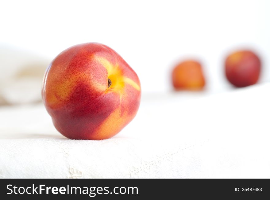 One nectarine with two out of focus in background on white napkin and against white background. One nectarine with two out of focus in background on white napkin and against white background