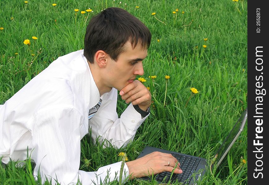 Young businessman with laptop lying on the grass