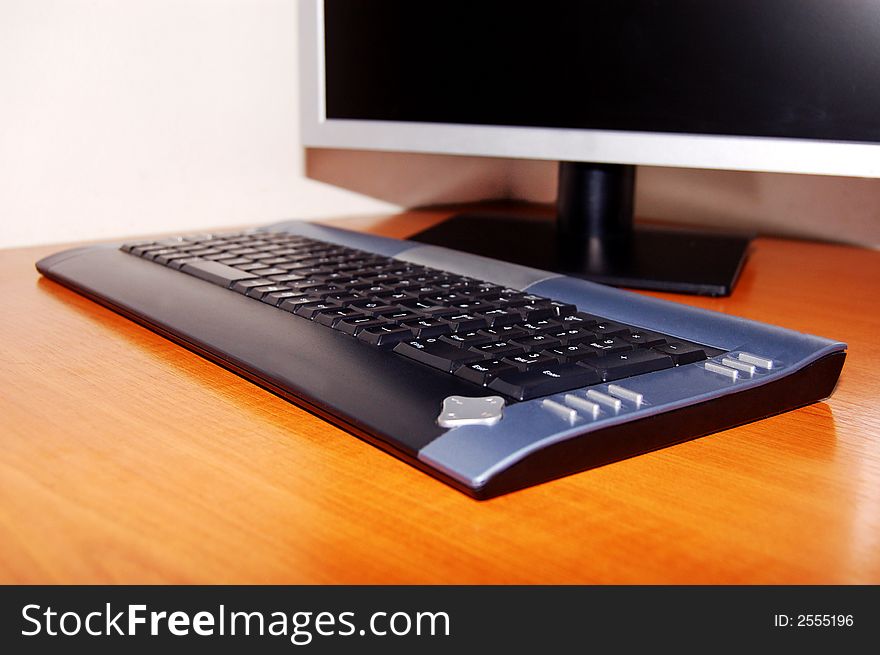 Black/dark grey computer keyboard, focus on keyboard and monitor out of focus. Black/dark grey computer keyboard, focus on keyboard and monitor out of focus