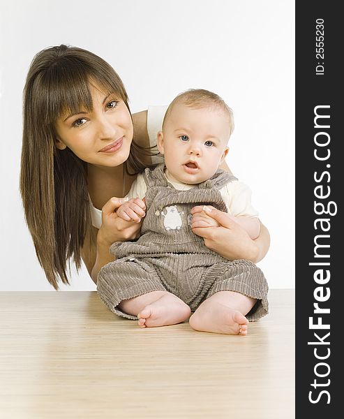 Young mother with baby boy. Baby is sitting on table. They looking at camera. Front view. Young mother with baby boy. Baby is sitting on table. They looking at camera. Front view