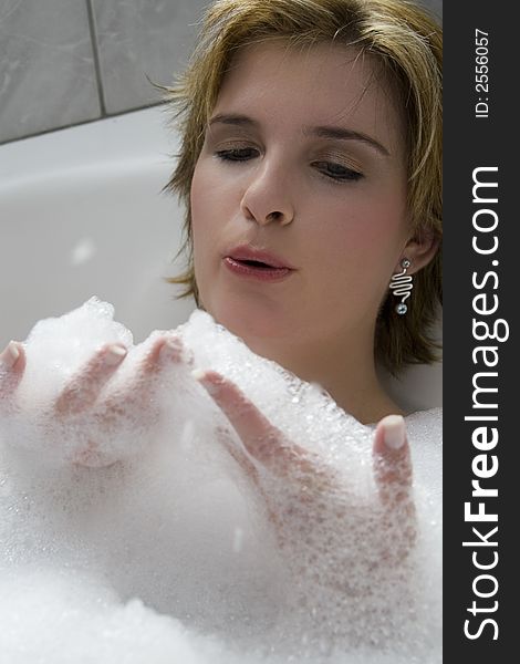 Attractive blond woman lying in bath blowing her bubble bath away. Attractive blond woman lying in bath blowing her bubble bath away
