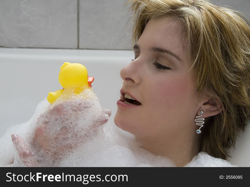 Attractive blond woman lying in bubble bath kissing her rubber ducky. Attractive blond woman lying in bubble bath kissing her rubber ducky