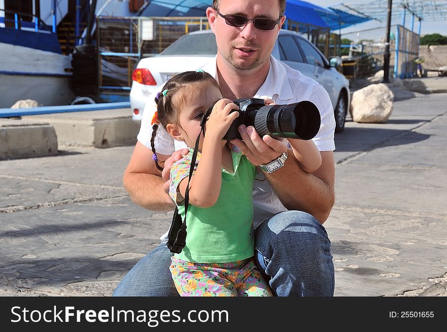 Dad teaches his daughter to photograph their camera, and maintains its bottom. Dad teaches his daughter to photograph their camera, and maintains its bottom