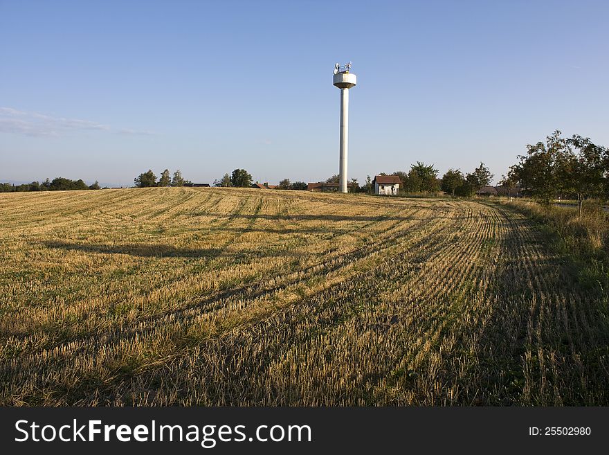 Harvested field with water tank in the background