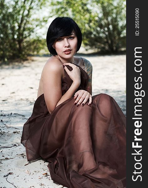 Beautiful black haired girl with tattoo wrapped in brown cloth stands in the tree shade in a desert. Beautiful black haired girl with tattoo wrapped in brown cloth stands in the tree shade in a desert