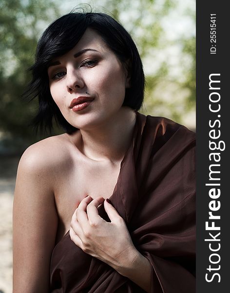 Beautiful black haired girl wrapped in brown cloth stands in the tree shade in a desert. Beautiful black haired girl wrapped in brown cloth stands in the tree shade in a desert