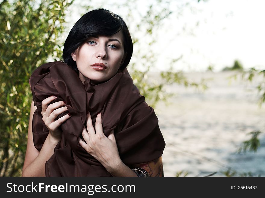 Beautiful black haired girl wrapped in brown cloth stands in the tree shade in a desert. Beautiful black haired girl wrapped in brown cloth stands in the tree shade in a desert