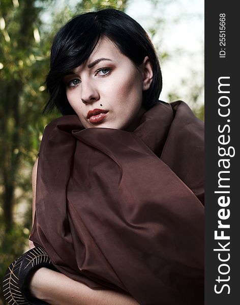 Beautiful black haired girl wrapped in brown cloth stands in the tree shade in a desert. Beautiful black haired girl wrapped in brown cloth stands in the tree shade in a desert