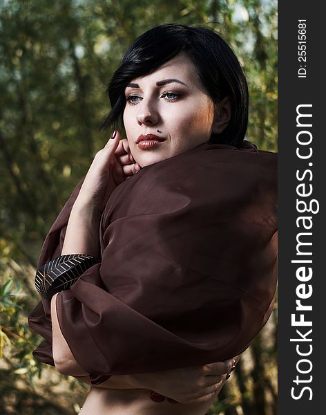 Beautiful black haired girl wrapped in brown cloth stands in the tree shade in a desert. Beautiful black haired girl wrapped in brown cloth stands in the tree shade in a desert