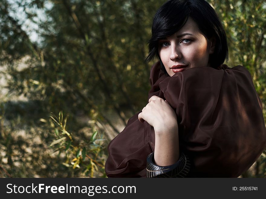 Beautiful black haired girl wrapped in brown cloth stands in the tree shade in a desert. Beautiful black haired girl wrapped in brown cloth stands in the tree shade in a desert