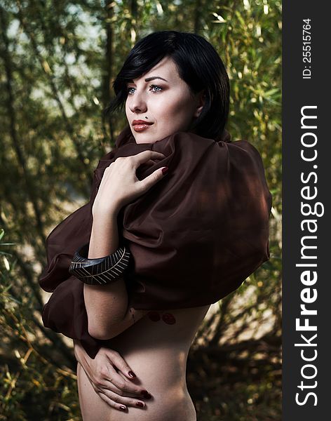 Beautiful black haired girl with tattoo wrapped in brown cloth stands in the tree shade in a desert. Beautiful black haired girl with tattoo wrapped in brown cloth stands in the tree shade in a desert