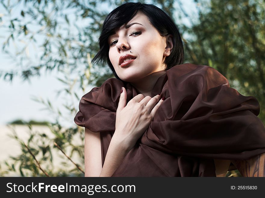 Beautiful black haired girl with tattoo wrapped in brown cloth stands in the tree shade in a desert. Beautiful black haired girl with tattoo wrapped in brown cloth stands in the tree shade in a desert