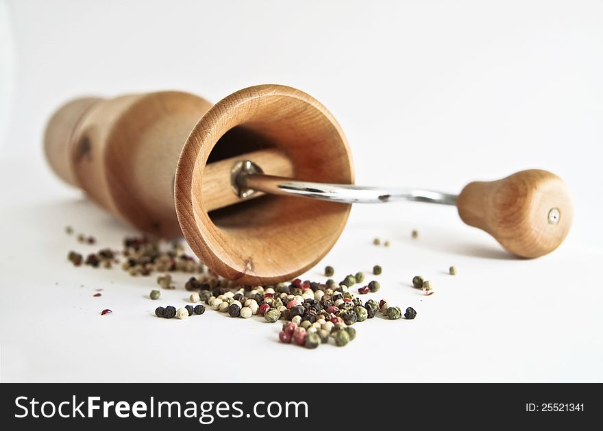 A wooden peppermill with peppercorns on white background