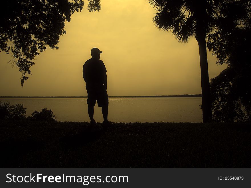 A man gazes out at the water in silhouette. A man gazes out at the water in silhouette.