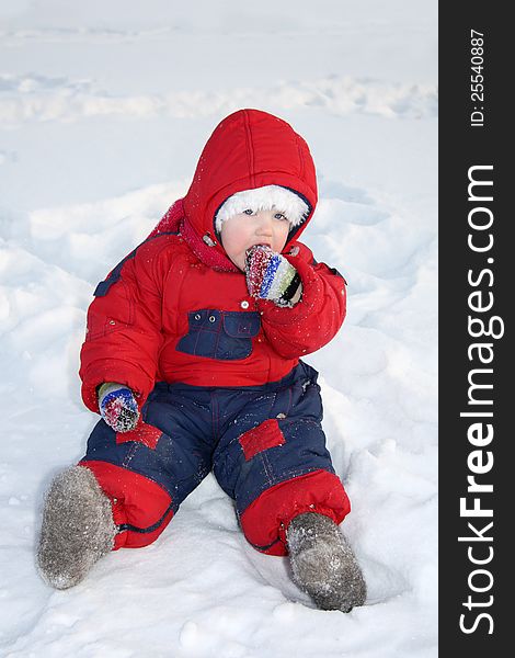 Little girl wearing warm jumpsuit sits on snow and eats snow at winter. Little girl wearing warm jumpsuit sits on snow and eats snow at winter