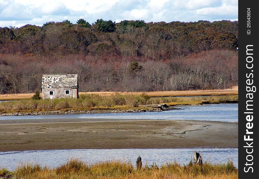 Old weathered little fishing cabin sitting on a sandy shore during low tides in the salt marsh.