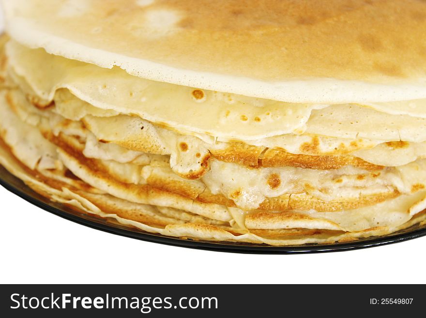 A stack of Russian thin pancakes on a dark plate isolated on white background. Close up. A stack of Russian thin pancakes on a dark plate isolated on white background. Close up.