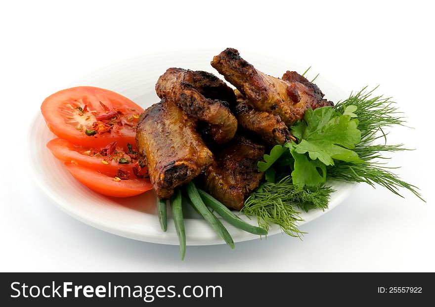 Barbecued pork ribs with tomato and greens on plate isolated on white background. Barbecued pork ribs with tomato and greens on plate isolated on white background