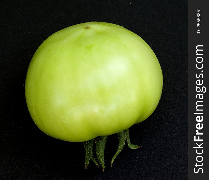 Green, raw tomato on black platform. Green, raw tomato on black platform.