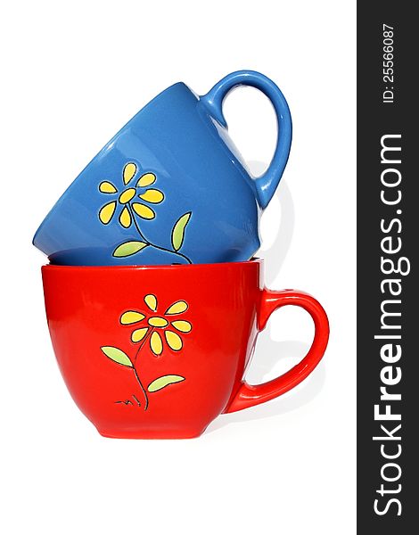 Red and dark blue mugs with yellow flower on white background. Photo.