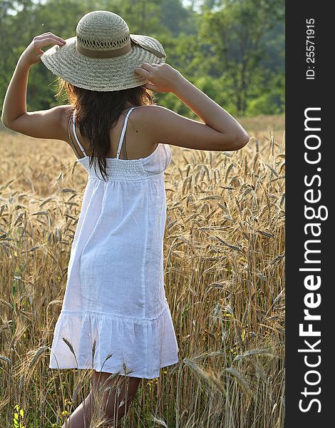 Young girl with hay hat in a wheat field from behind . Sunset drama light