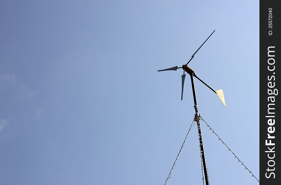 Bright blue sky and the blades of a wind generator standing tall in the yard of a countryside home.