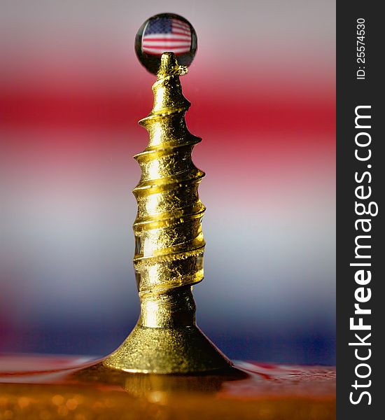 A waterdrop caught as it hits a screw. The drop has an image of the USA flag refracted through it. A waterdrop caught as it hits a screw. The drop has an image of the USA flag refracted through it