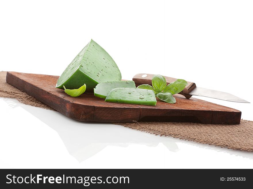 Green cheese gouda with pesto on dark brown chopping board with fresh basil leaf and knife. Minimal cheese still life. Green cheese gouda with pesto on dark brown chopping board with fresh basil leaf and knife. Minimal cheese still life.