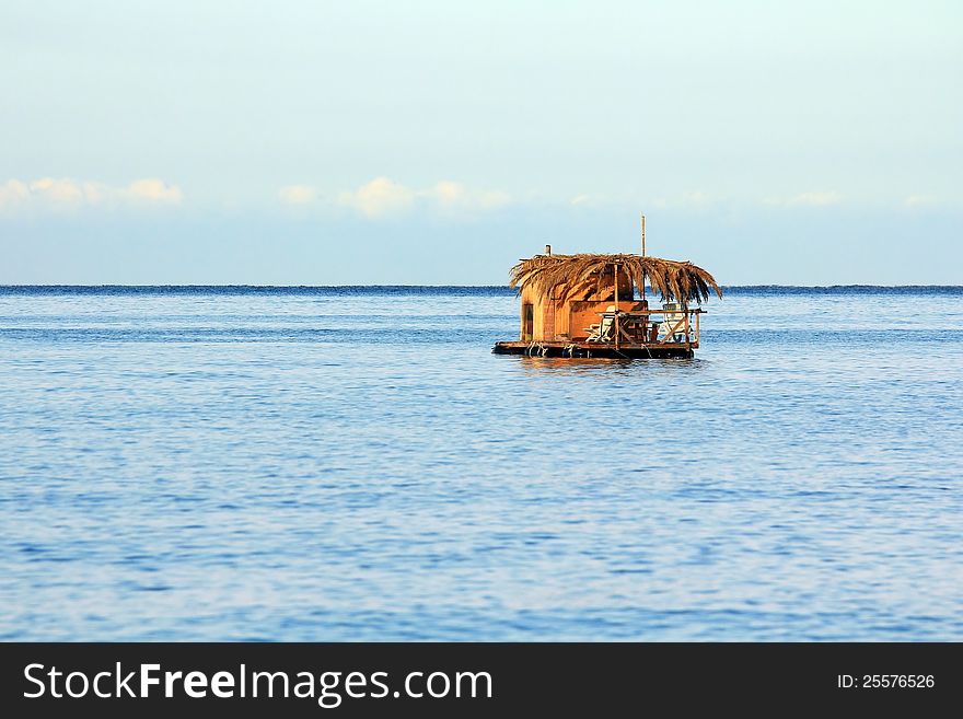 Single houseboat on a small raft at open sea under blue clear sky. Single houseboat on a small raft at open sea under blue clear sky